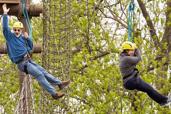 A man and a woman ride a zip line through the trees