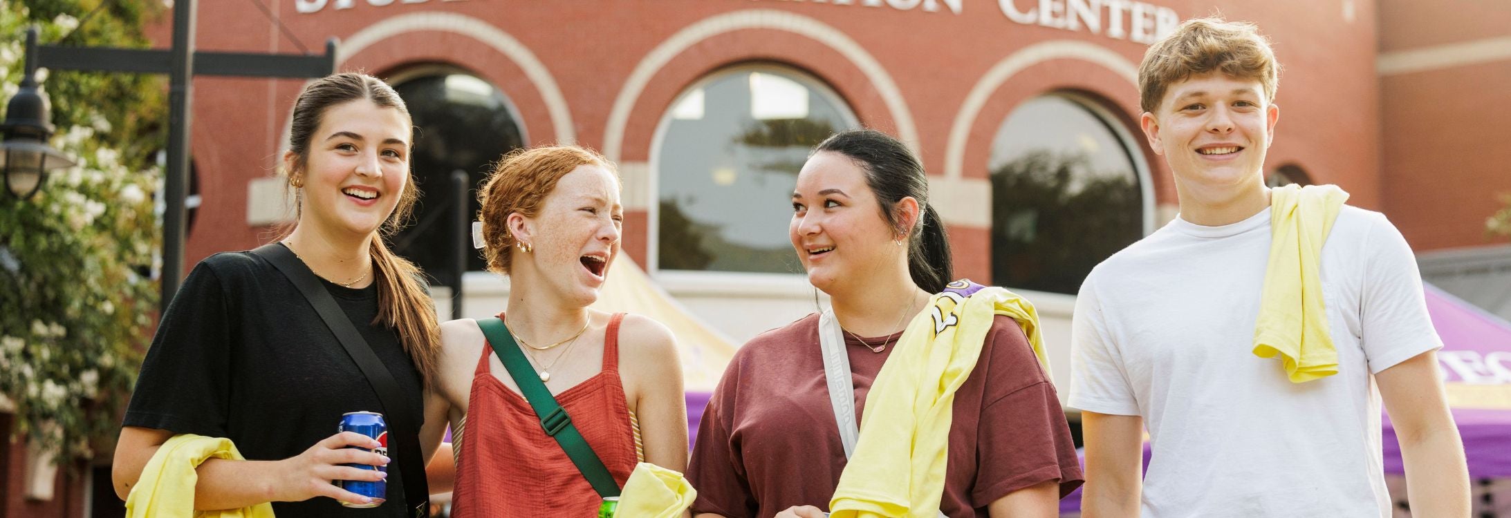 A group of four students laugh and walk side-by-side as they leave the Eakin Student Recreation Center on campus.